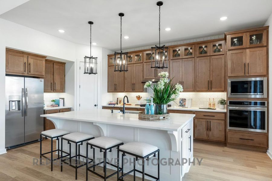 Kitchen featuring light countertops, light wood-type flooring, backsplash, appliances with stainless steel finishes, and brown cabinets