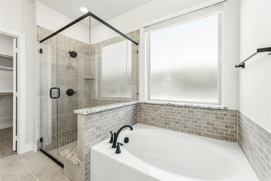 Master bathroom with soaking tub, glass-enclosed shower, gray tile walls, and frosted window