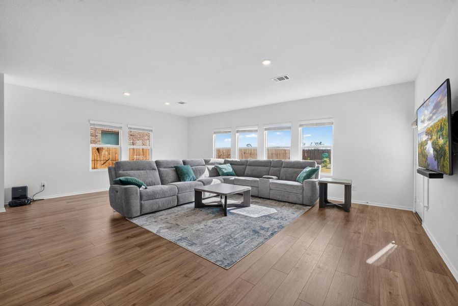 A spacious living room featuring warm wood flooring and ample natural light through a series of broad windows. A spacious living room featuring warm wood flooring and ample natural light through a series of broad windows.