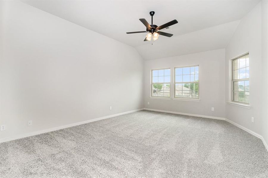 Carpeted empty room with plenty of natural light, lofted ceiling, and ceiling fan