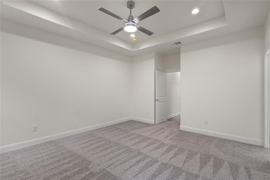 Spacious room featuring a tray ceiling with recessed lighting and a ceiling fan, light gray patterned carpet, white baseboards, and a white interior door Spacious room featuring a tray ceiling with recessed lighting and a ceiling fan, light gray patterned carpet, white baseboards, and a white interior door