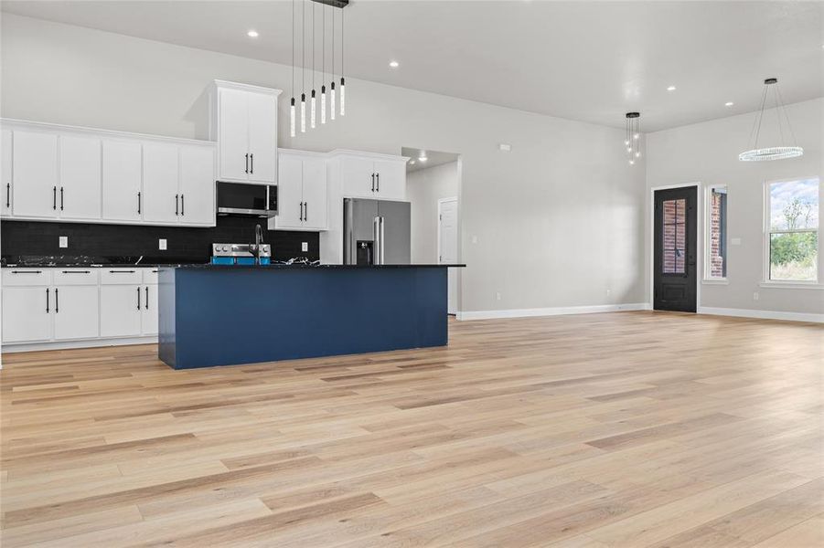 Kitchen with dark countertops, white cabinetry, backsplash, open floor plan, and a kitchen island with sink