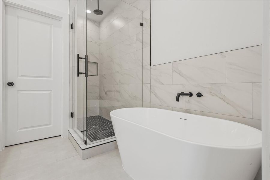 Luxurious primary bathroom showcasing a relaxing soaking tub and a spacious walk-in shower with a sleek glass enclosure and rainfall shower head. Designed for both comfort and indulgence, this spa-like retreat invites you to unwind in style.