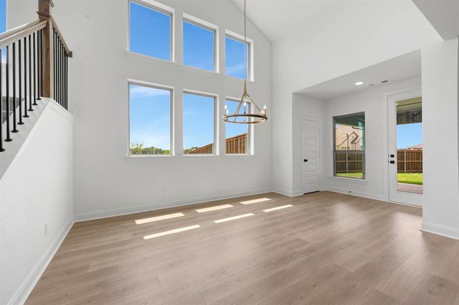 Vaulted ceiling interior space featuring wood-finish flooring, a contemporary chandelier, multiple large windows, and a glass-paneled door