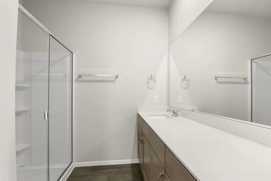 Image of a bathroom with brown wood-like flooring and white vanity with mirror and a walk-in shower