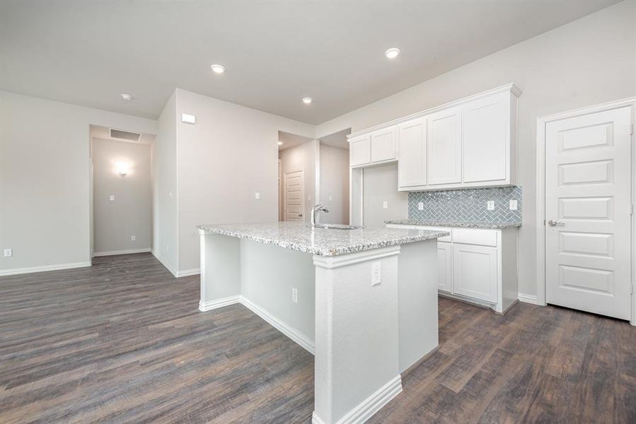 Kitchen featuring dark wood-type flooring, a center island with sink, white cabinets, sink, and tasteful backsplash