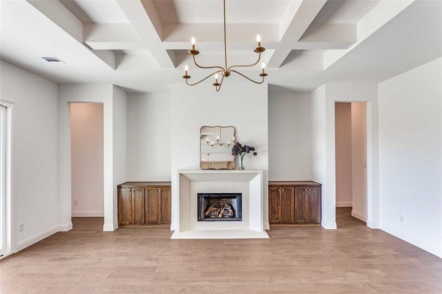 Unfurnished living room featuring coffered ceiling, beamed ceiling, light wood-style floors, a fireplace, and a chandelier Unfurnished living room featuring coffered ceiling, beamed ceiling, light wood-style floors, a fireplace, and a chandelier