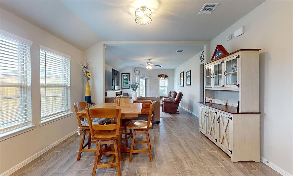 Featuring wood-look tile flooring, the dining space accommodates a wooden table with four chairs, and large windows provide ample natural light.