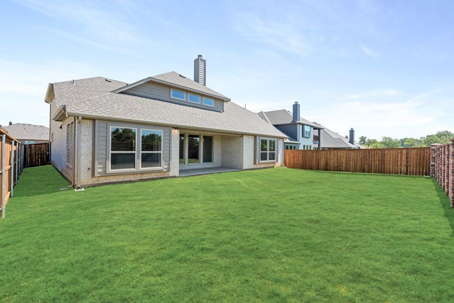 Brick home rear exterior with large fenced backyard, patio, and green lawn
