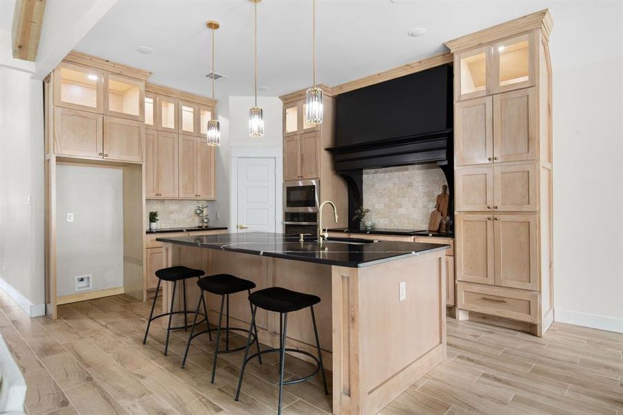 Kitchen featuring decorative light fixtures, stainless steel appliances, light hardwood / wood-style floors, an island with sink, and decorative backsplash