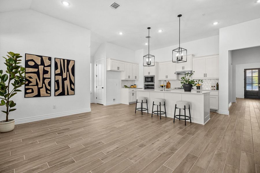 Kitchen with a kitchen bar, decorative backsplash, hanging light fixtures, a center island with sink, and white cabinets