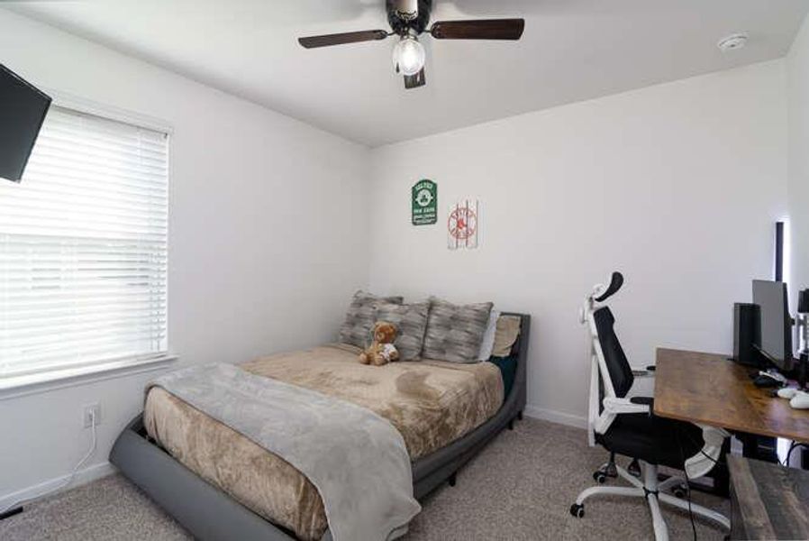 Carpeted bedroom featuring multiple windows, an office area, and a ceiling fan