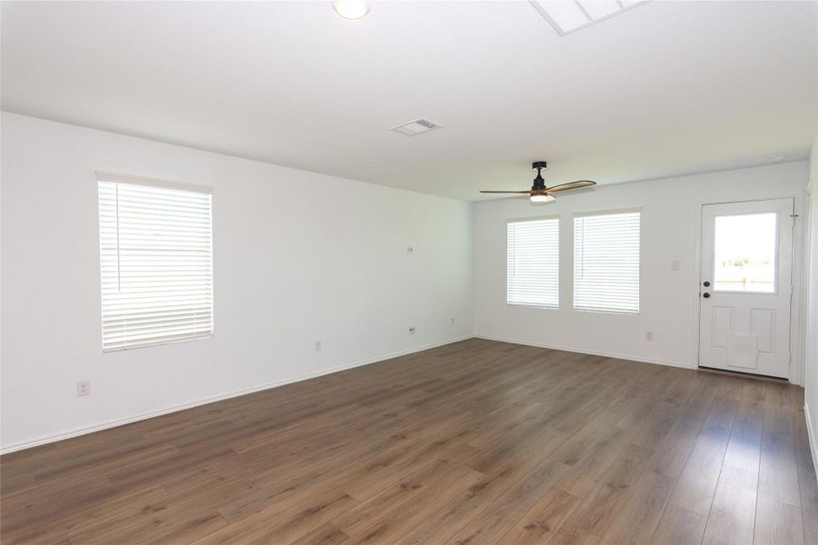 Expansive living room featuring wood-finish flooring, multiple windows with blinds, a ceiling fan, and a rear exterior door
