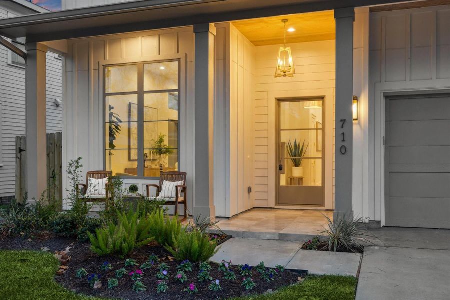 The home’s exterior features custom antique brass house numbers, a neutral color palette, and a beautifully landscaped yard, highlighted by a substantial metal grid-style glass front door.