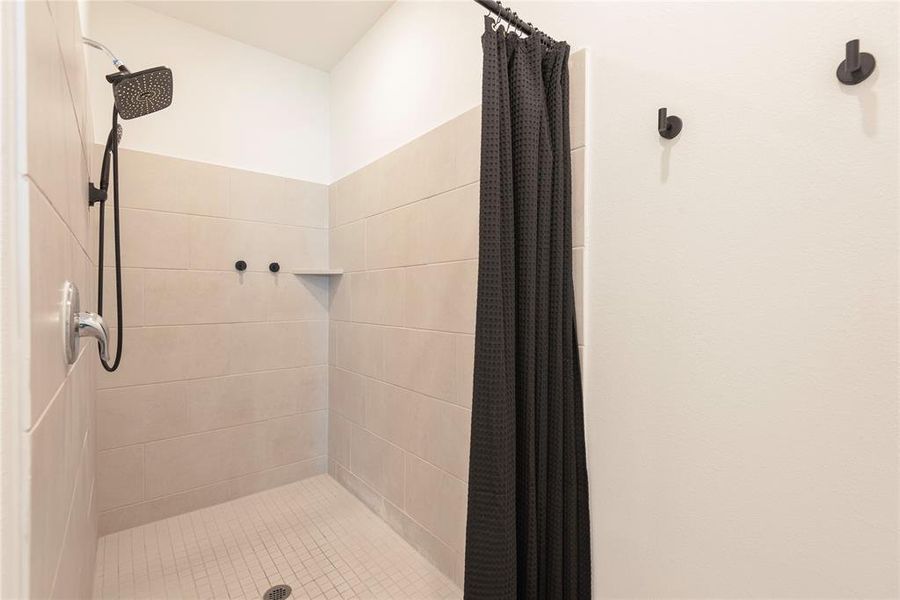 Shower stall featuring light-toned tile walls and floor, a built-in shower niche, and a contrasting dark shower head Shower stall featuring light-toned tile walls and floor, a built-in shower niche, and a contrasting dark shower head