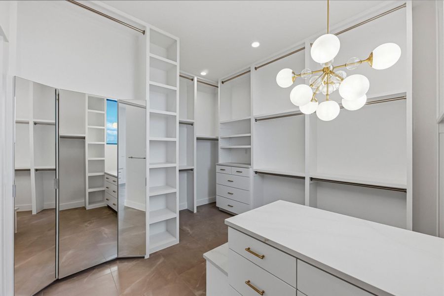 Primary walk in closet with peninsula, storage behind mirrors, bench and natural lighting.
