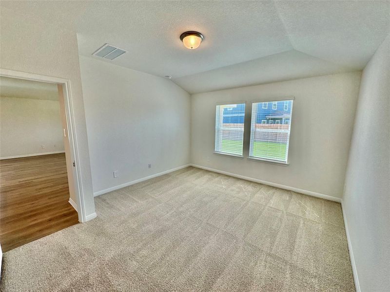 Empty room featuring light colored carpet, vaulted ceiling, and a textured ceiling