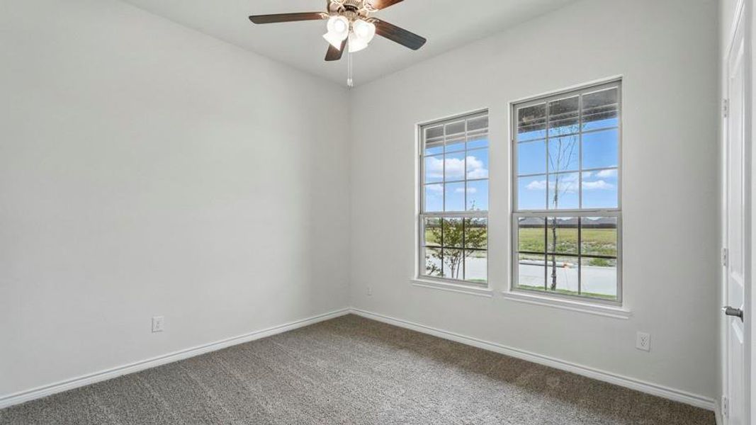 Carpeted room featuring two gridded windows, a ceiling fan with integrated lighting, and white baseboards