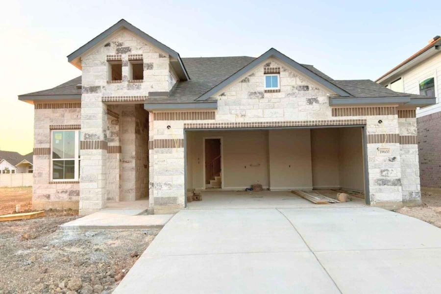View of front of house featuring stone siding, concrete driveway, and a shingled roof
