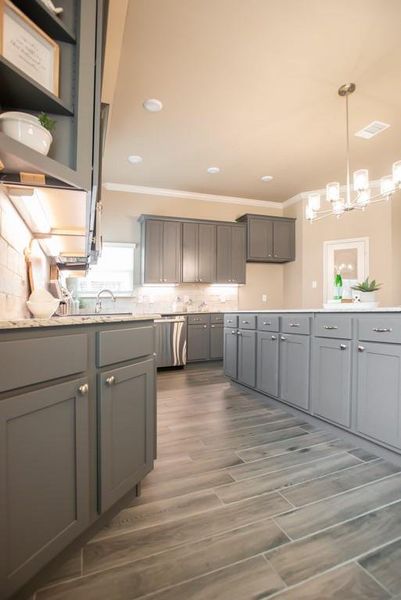 Kitchen with gray cabinets, ornamental molding, tasteful backsplash, light countertops, and dark wood-style floors Kitchen with gray cabinets, ornamental molding, tasteful backsplash, light countertops, and dark wood-style floors