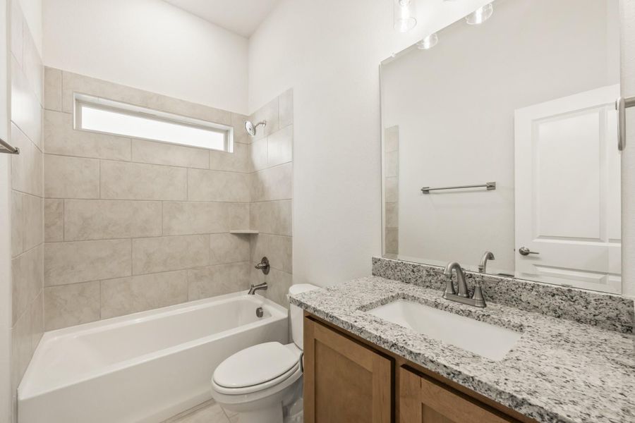 Bathroom with granite vanity, tiled tub surround, and small window above the bathtub Bathroom with granite vanity, tiled tub surround, and small window above the bathtub