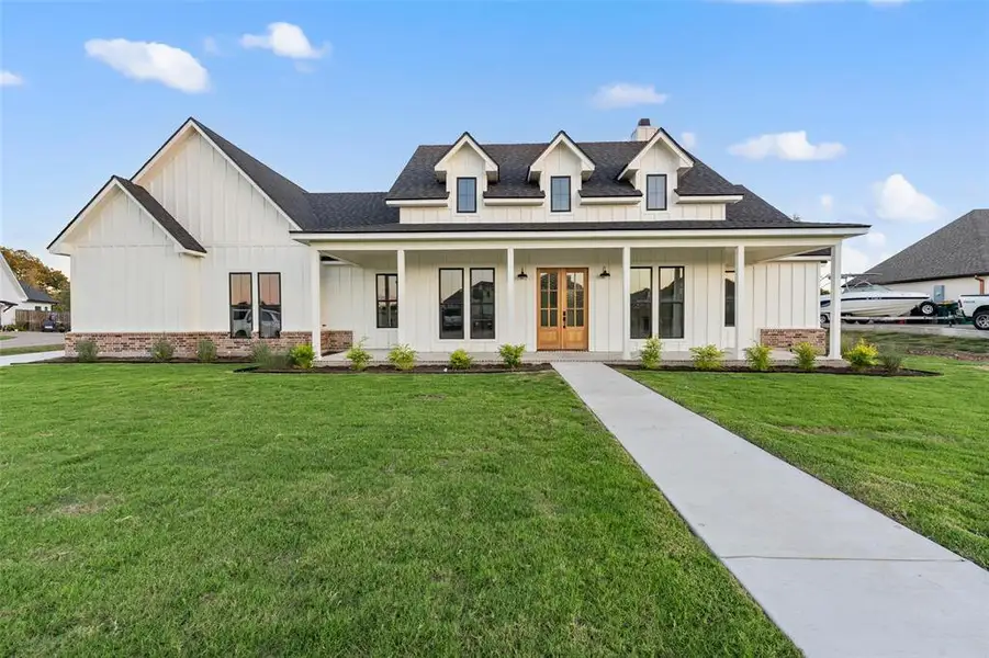 Modern farmhouse style home with board and batten siding, a shingled roof, a front lawn, covered porch, and a chimney Modern farmhouse style home with board and batten siding, a shingled roof, a front lawn, covered porch, and a chimney