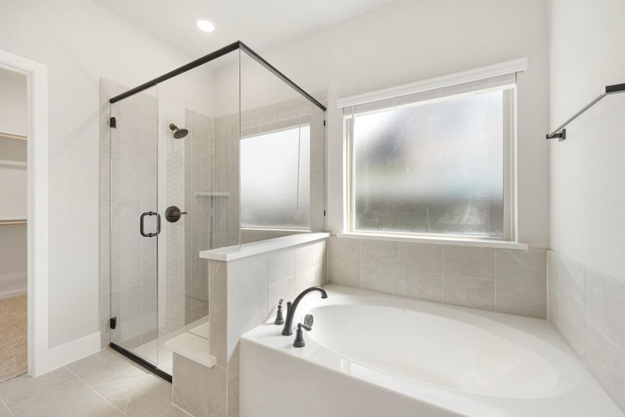 Bathroom with soaking tub, glass-enclosed shower, gray tile, and frosted window near walk-in closet entry