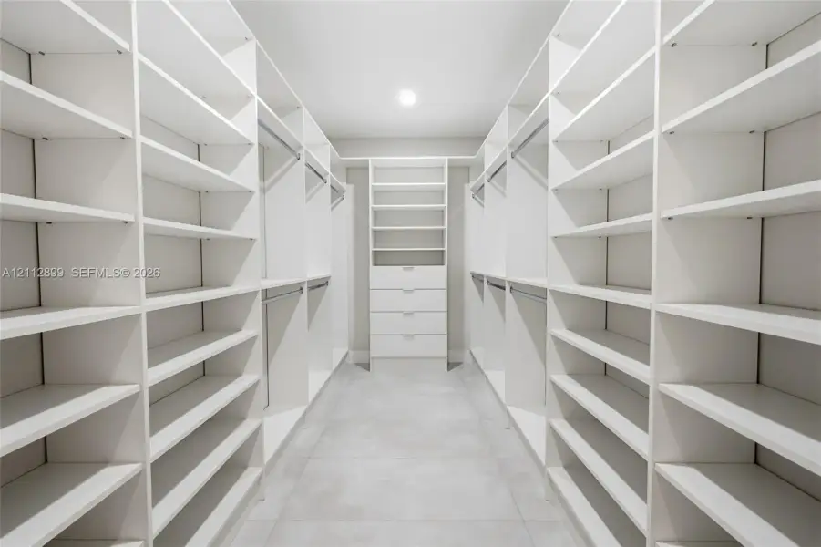 Walk-in closet featuring extensive built-in white shelving, integrated clothing rods, a central drawer bank, and tile flooring