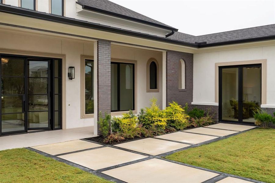 Doorway to property featuring brick siding, a shingled roof, a lawn, and stucco siding