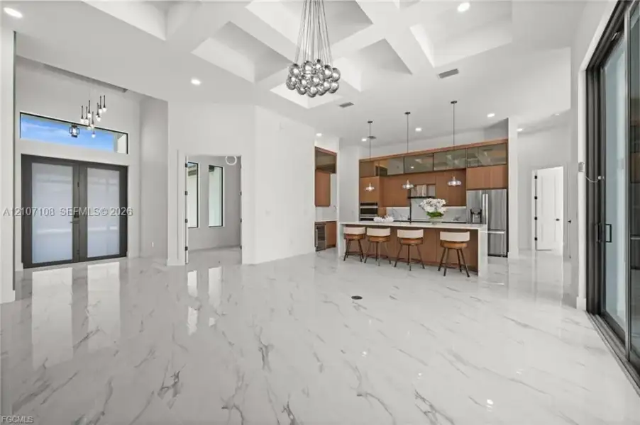 Coffered ceilings featuring recessed lighting, polished stone-finish flooring, custom cabinetry with integrated stainless steel appliances, large kitchen island with quartz countertops, and floor-to-ceiling glass sliding doors
