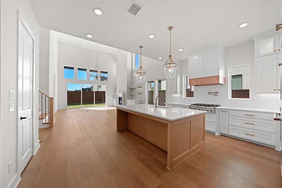 Kitchen with white cabinetry, light wood finished floors, a kitchen island with sink, recessed lighting, and pendant lighting Kitchen with white cabinetry, light wood finished floors, a kitchen island with sink, recessed lighting, and pendant lighting