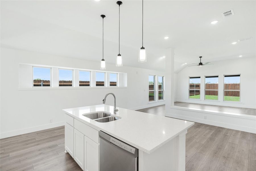 Kitchen island with white quartz countertop, double sink, and pendant lights open to living area with hardwood floors.