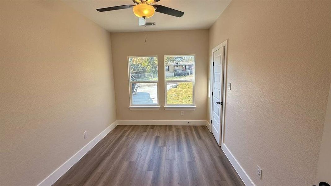 Empty room with dark wood finished floors, a textured wall, and a ceiling fan