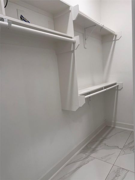 Spacious walk-in closet featuring sleek shelving and ample hanging space, complemented by elegant tile flooring. Spacious walk-in closet featuring sleek shelving and ample hanging space, complemented by elegant tile flooring.