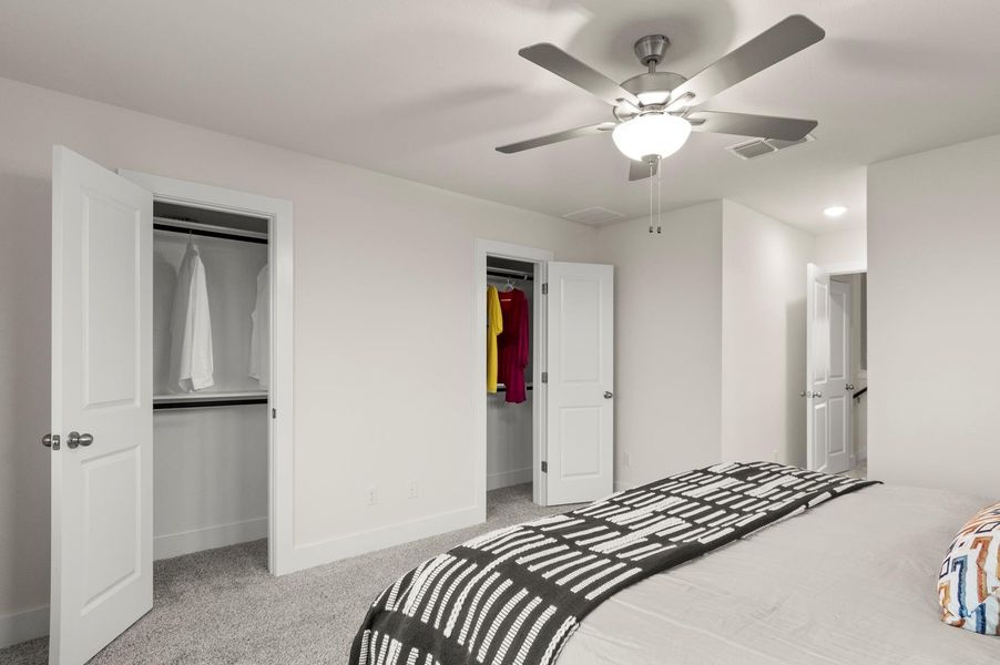 A well-lit bedroom features plush carpeting and a modern ceiling fan, offering comfortable living.