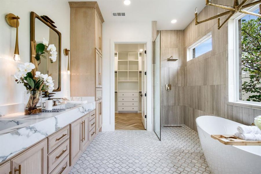 Spacious bathroom featuring a dual vanity with marble countertops, a freestanding soaking tub, a glass-enclosed shower, and patterned floor tiling Spacious bathroom featuring a dual vanity with marble countertops, a freestanding soaking tub, a glass-enclosed shower, and patterned floor tiling