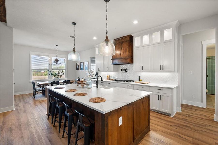 Kitchen featuring white cabinetry, decorative backsplash, a kitchen breakfast bar, light stone counters, and recessed lighting Dining area in sight