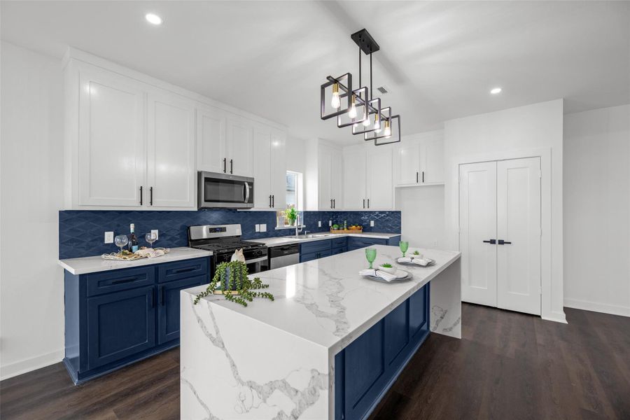 Elegant kitchen with sleek white and blue cabinetry, marble countertops, and a central island. Features a stylish light fixture, stainless steel appliances, and dark wood flooring. Ideal for entertaining.