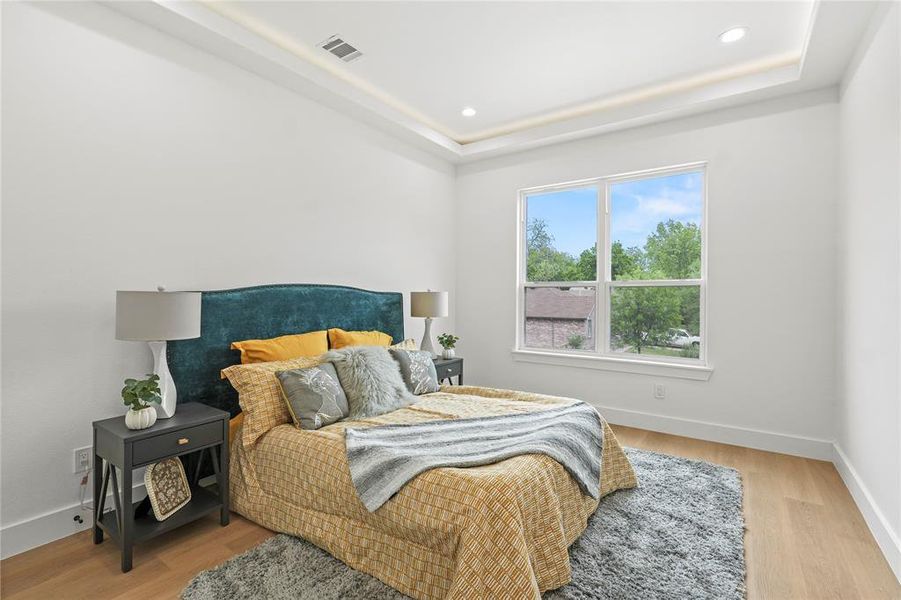 Bedroom with light wood finished floors, baseboards, visible vents, and a tray ceiling