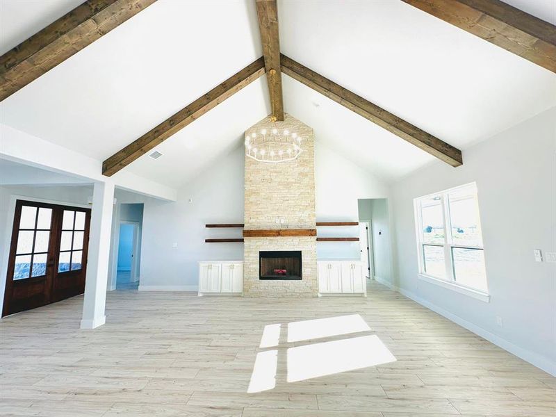 Unfurnished living room with a fireplace, french doors, high vaulted ceiling, and light wood-type flooring