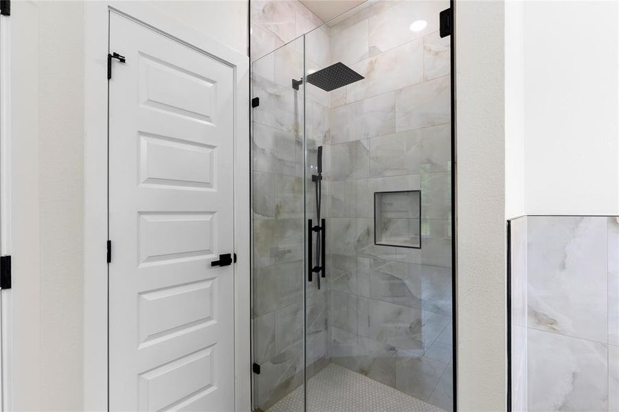 Frameless glass shower enclosure with matte black hardware, integrated niche, and patterned wall tiling