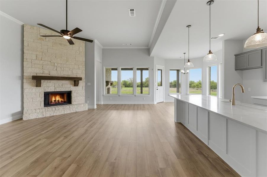 Unfurnished living room featuring light wood-style floors, a fireplace, ornamental molding, ceiling fan, and hanging lights