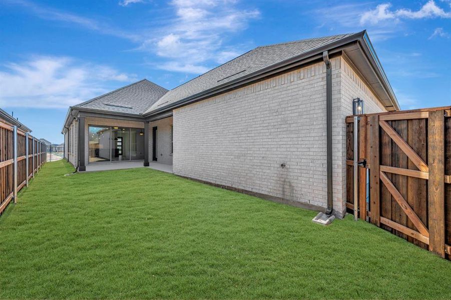 Rear view of house with brick siding, a fenced backyard, a gate, and a patio
