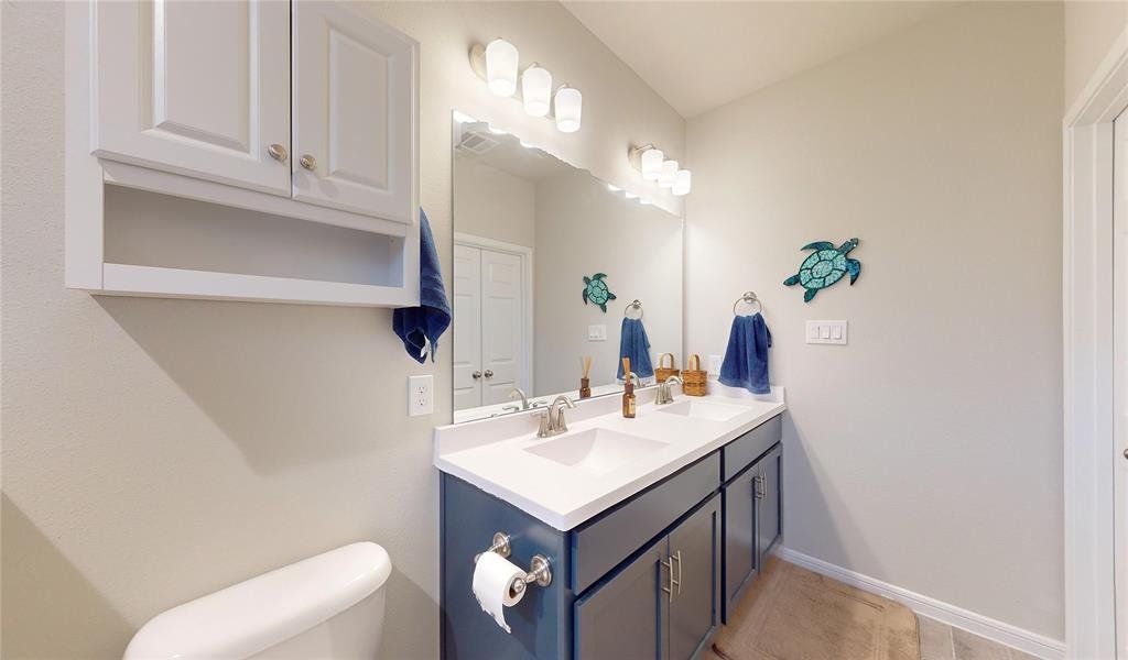 This photo shows a modern bathroom featuring a double sink vanity with sleek fixtures, ample lighting, and a large mirror.