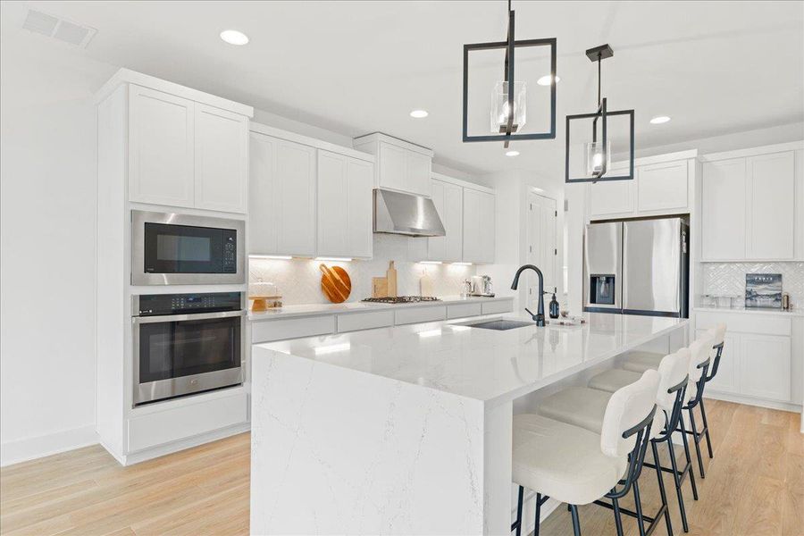Kitchen featuring stainless steel appliances, a kitchen breakfast bar, light wood-type flooring, hanging light fixtures, and white cabinets Kitchen featuring stainless steel appliances, a kitchen breakfast bar, light wood-type flooring, hanging light fixtures, and white cabinets