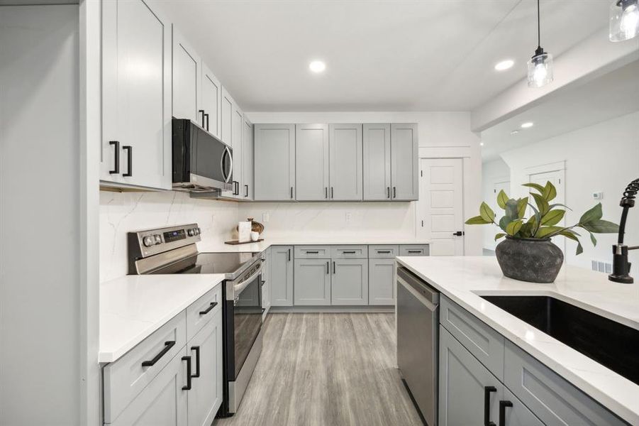 Kitchen with gray cabinetry, a center waterfall island with sink, stainless steel appliances and a pantry