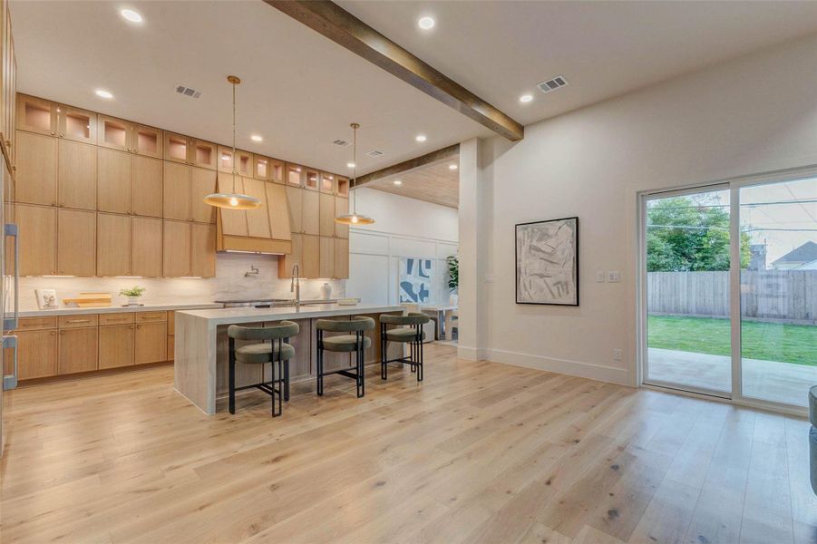 From the family room, the open layout flows effortlessly into the gourmet kitchen. A striking wood-beam ceiling, designer lighting, and a wall of cabinetry highlight the home’s craftsmanship and thoughtful design.