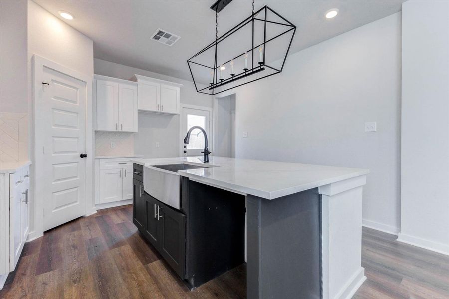 Sleek meets functional in this kitchen with a deep farmhouse sink, contrasting dark base cabinetry, and eye-catching matte black hardware. The bold rectangular light fixture above the island makes a statement, ideal for both meal prep and gathering with friends.