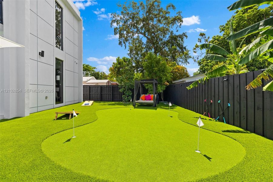 Private backyard featuring a synthetic grass putting green, solid-panel privacy fencing, and modern exterior wall cladding