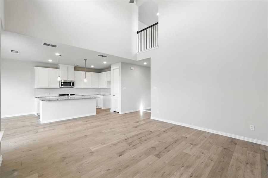 Unfurnished living room with light wood-style flooring, a towering ceiling, and recessed lighting Unfurnished living room with light wood-style flooring, a towering ceiling, and recessed lighting